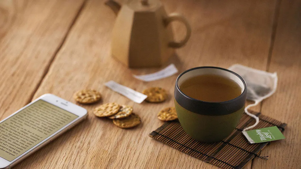 Tea cup with a phone, cookies, and teapot on a wooden table