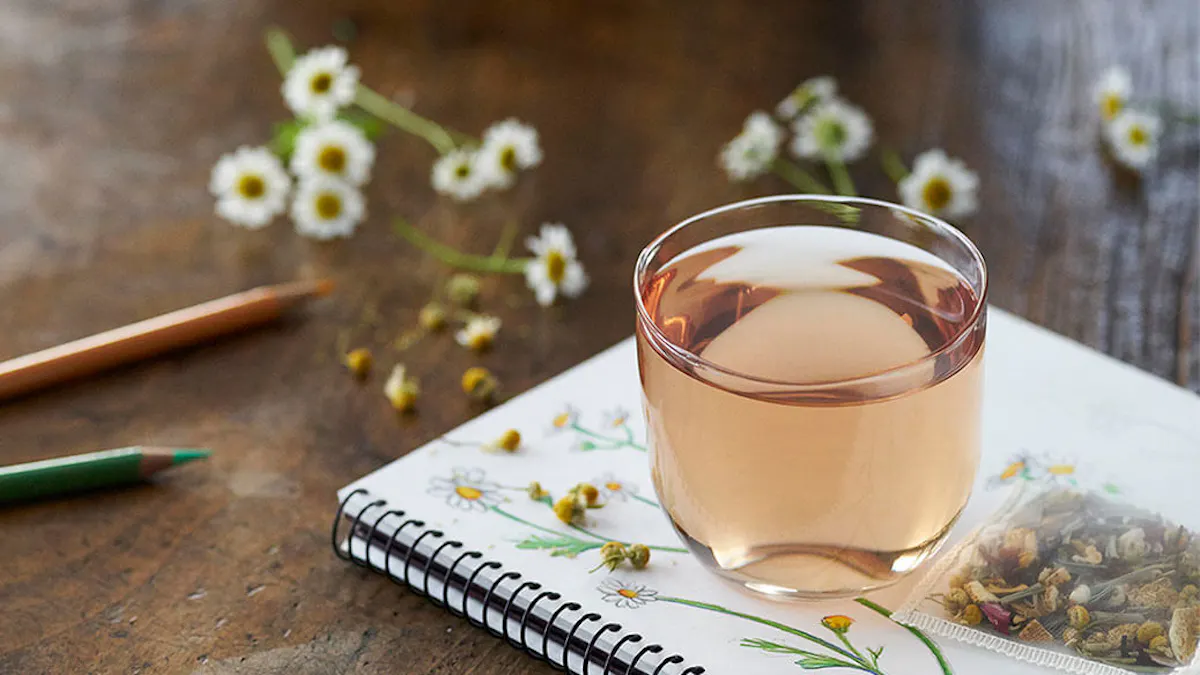 Glass of tea on a notebook with flowers and a pencil on a wooden surface