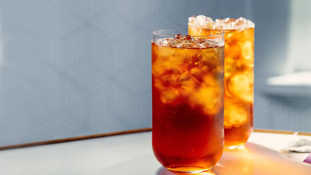 Two glasses of iced tea on a wooden surface with a light blue background