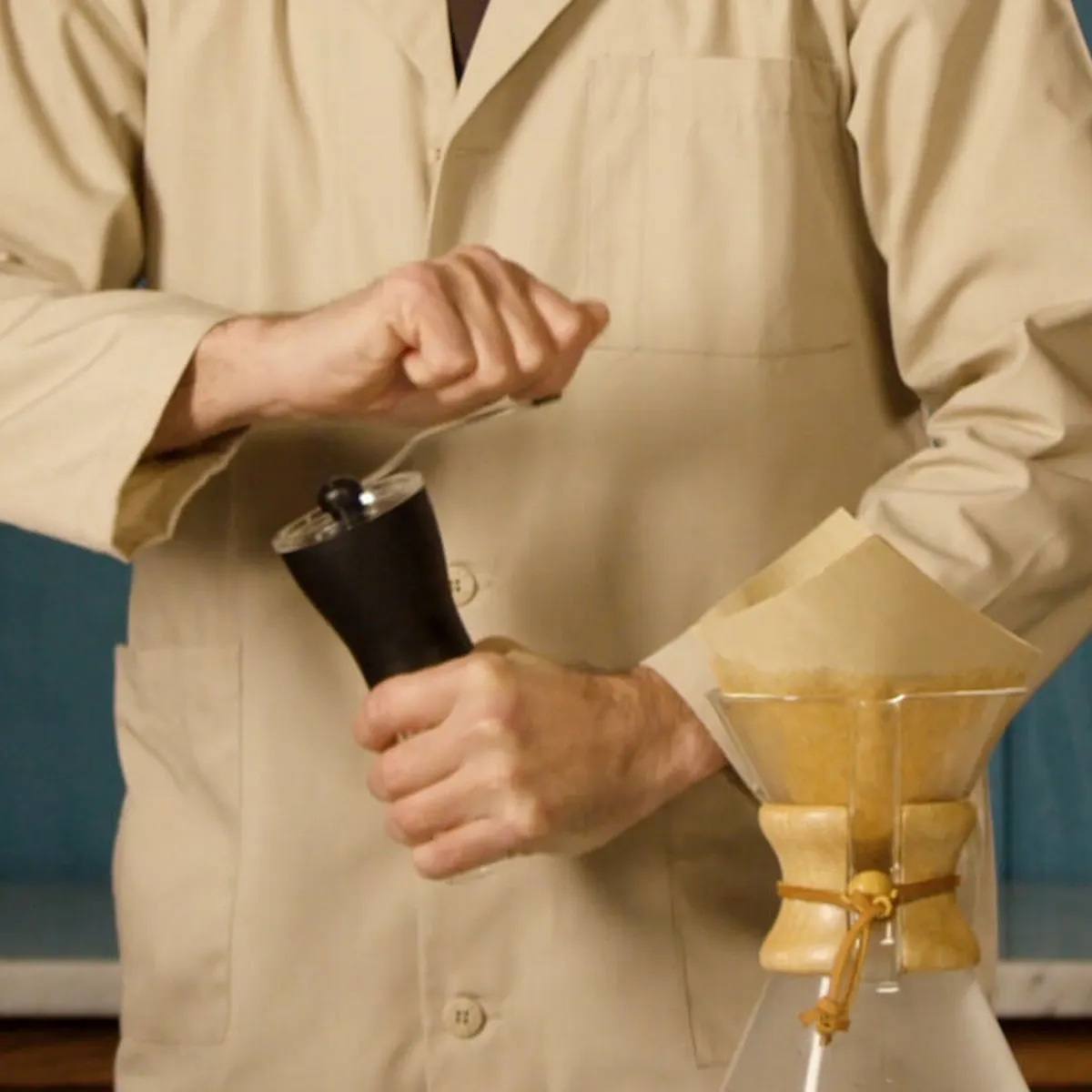 Person in a beige lab coat holding a black object with a blue background