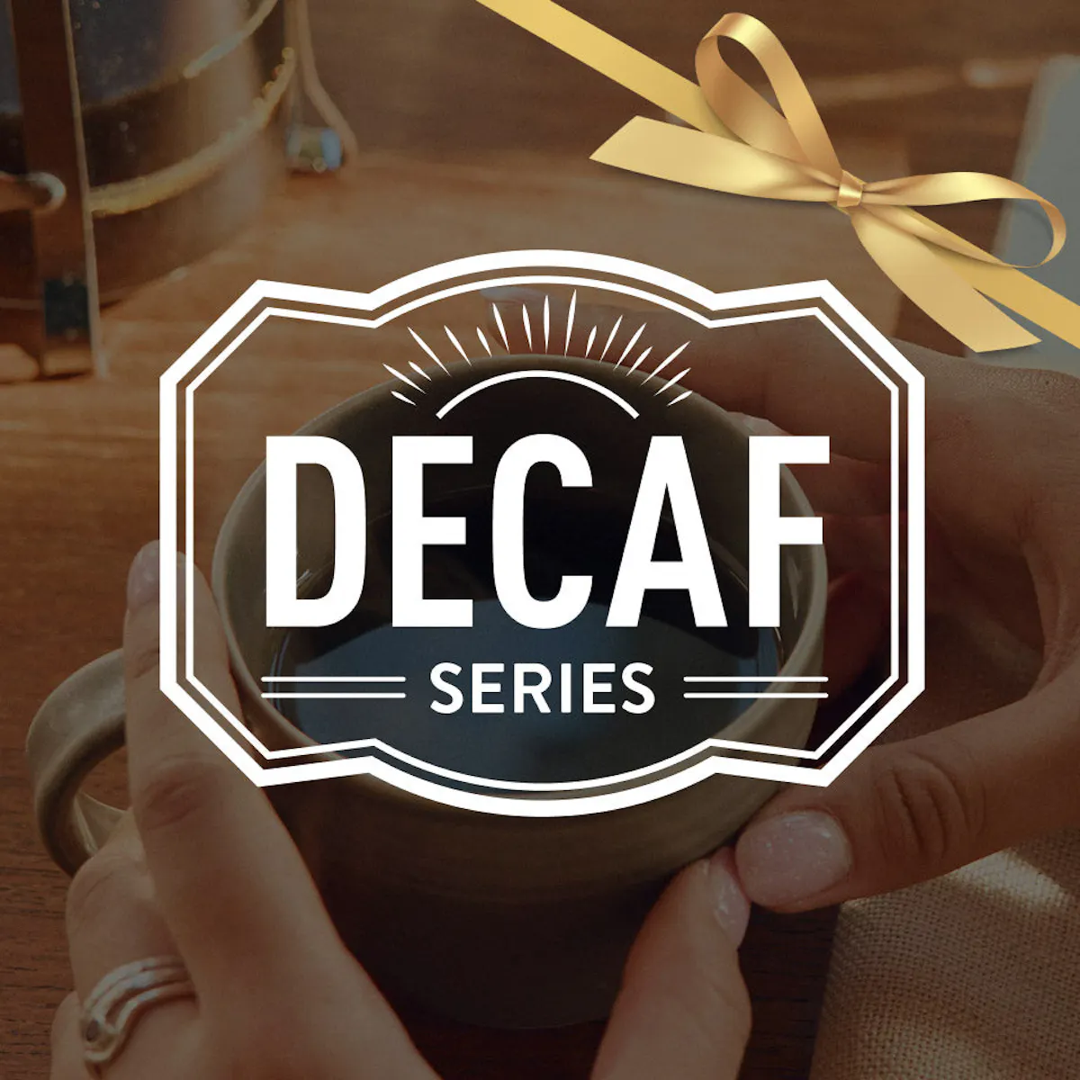 Person holding a  coffee cup with a decaf series banner and a decorative bow in the background